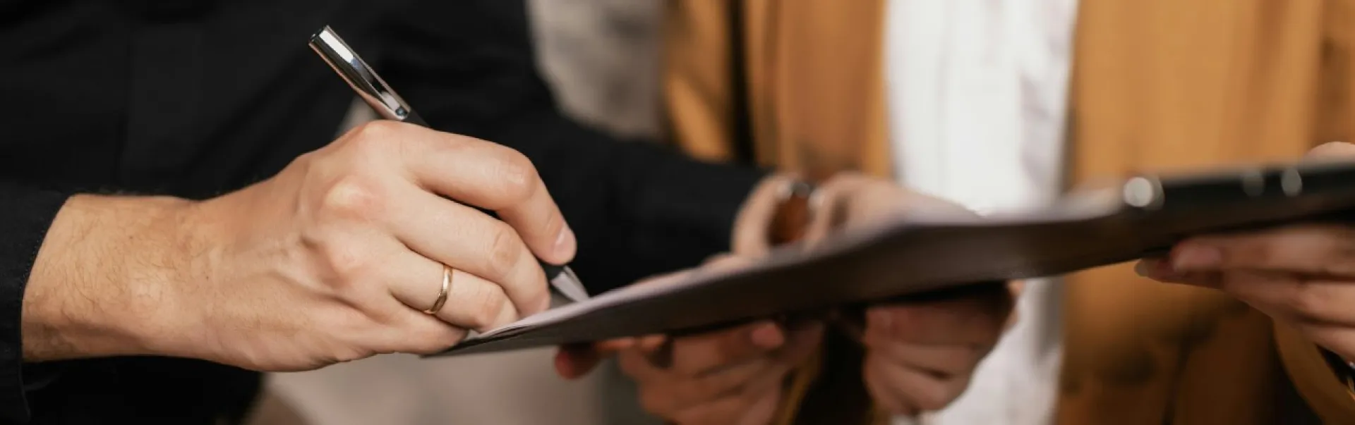 Someone signing a contract with a pen on a clipboard