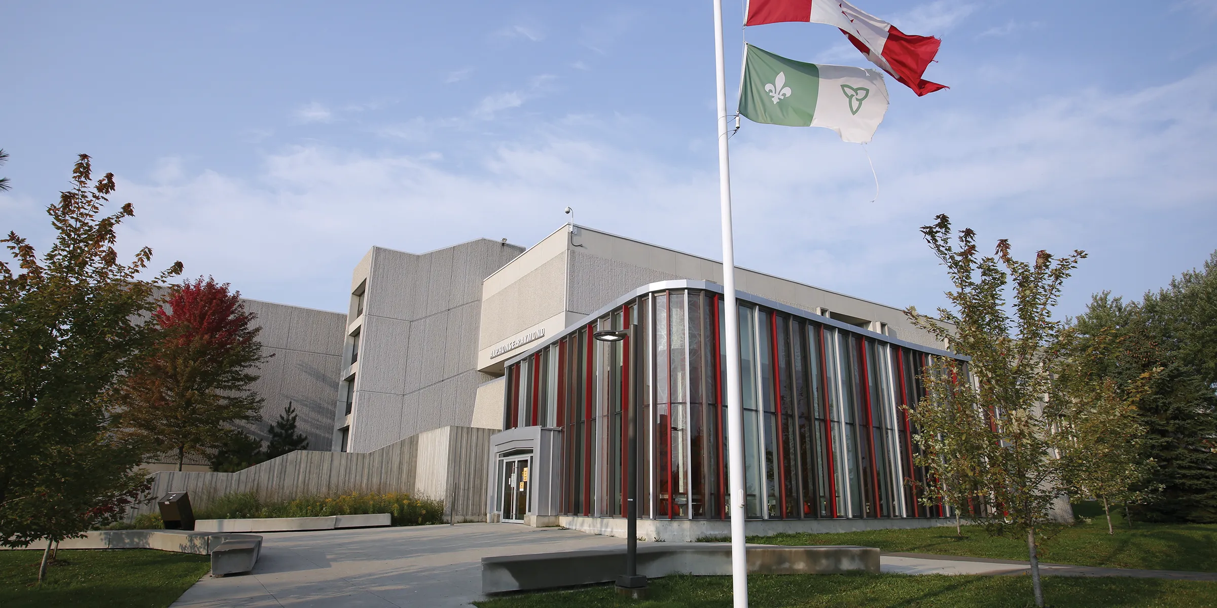 The Alphonse Raymond building with the Canadian and Franco-Ontarian flags flying on the flagpole outside.