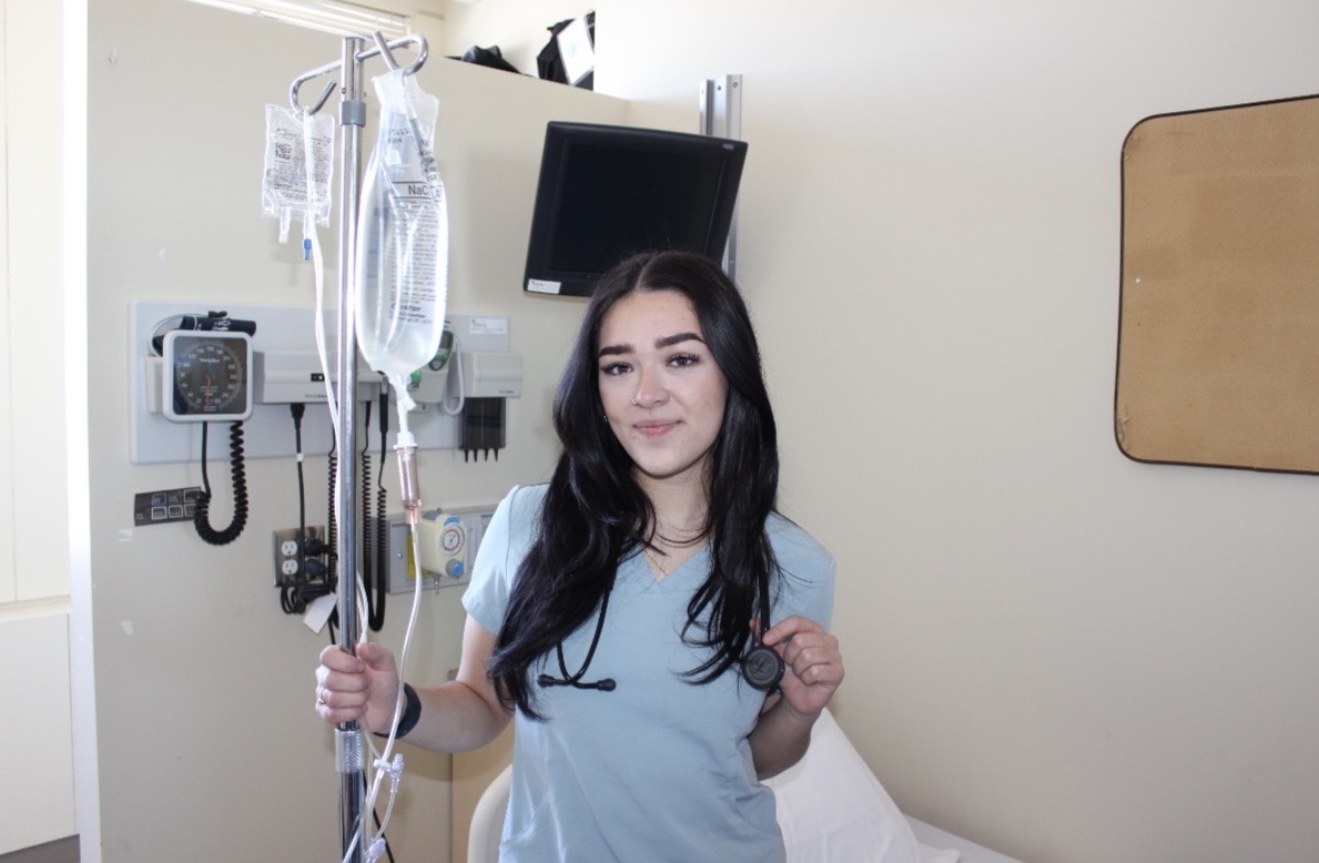 Erica Marrello, a third-year Bachelor of Science in Nursing student and Co-president of the French Nursing Council, stands in the Laurentian University nursing simulation lab holding an IV pole and her stethoscope.