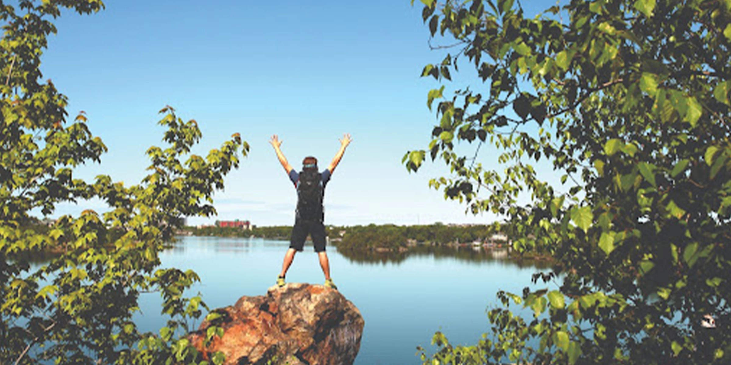 Hiker standing on top of a rock near a lake celebrating
